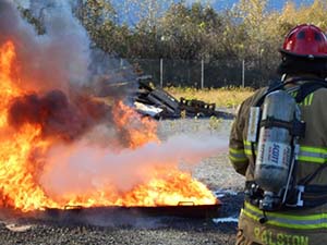 A firefighter practices on live fire in a controlled situation during the 2013 Marine Firefighting Symposium. Photo by Alan Sorum.