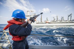 Photo shows Coast Guard officer firing a messenger shot line from one Coast Guard vessel to another. This is one method of connecting tow lines between a tug and a tanker.