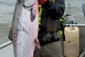 Gordon Terpening stands on a fishing boat, holding up a large salmon.