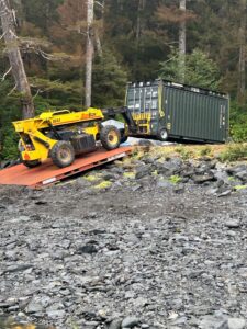 A large forklift carefully places a new conex on a concrete foundation. 