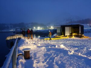 Photo shows responders practicing an oil spill response during low-light conditions. The area is lit using multiple bright lights to be able to see the equipment.