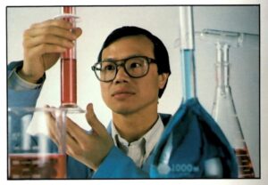 A young Greg Tang holds up a test tube which contains a substance he is analyzing.
