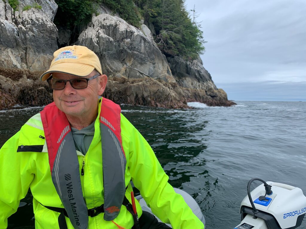 Photo of Tim Robertson on a small motorized boat on the ocean with a rocky coast in the background.