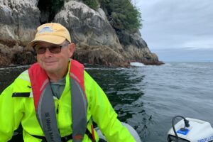 Photo of Tim Robertson on a small motorized boat on the ocean with a rocky coast in the background.