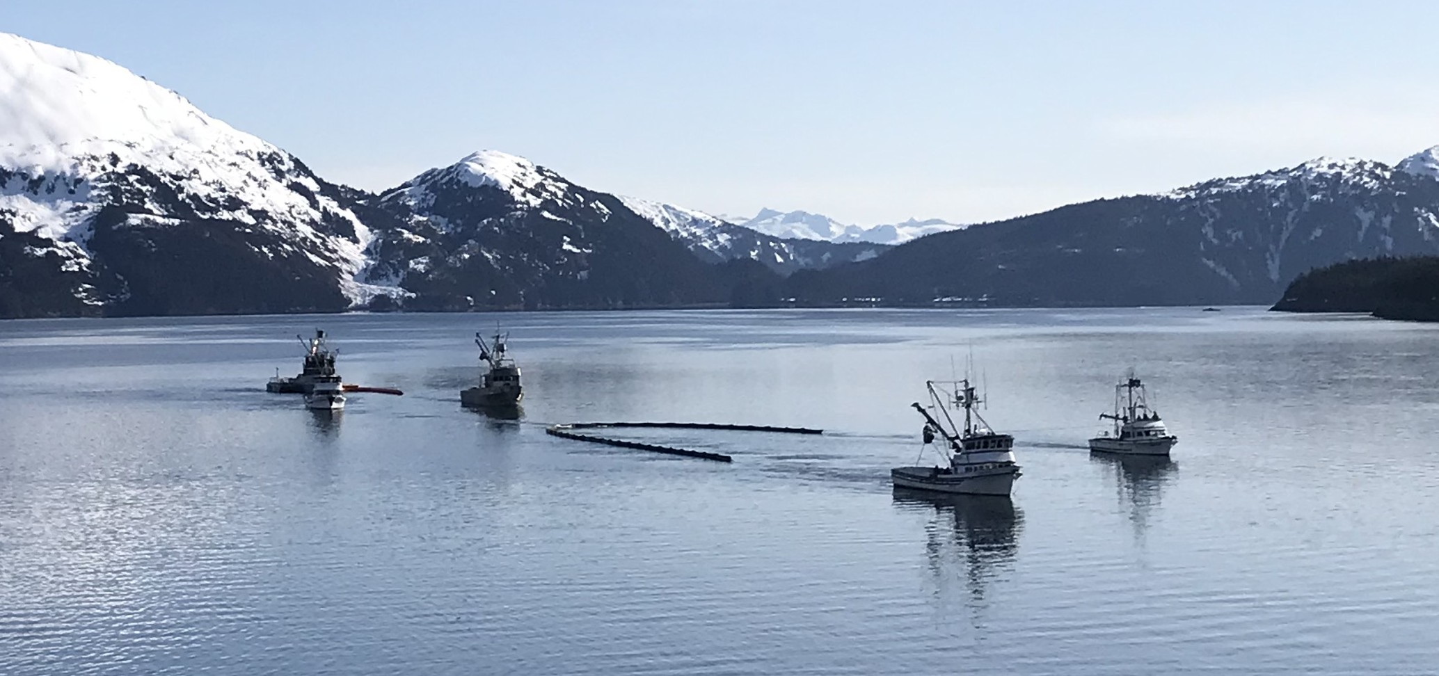 Two fishing vessels pull boom behind them. Each boat is attached to one end of the boom so that when they move forward, the boom forms a curve. In this first image, the boats are parallel with each other so that the boom is in the shape of the letter U.